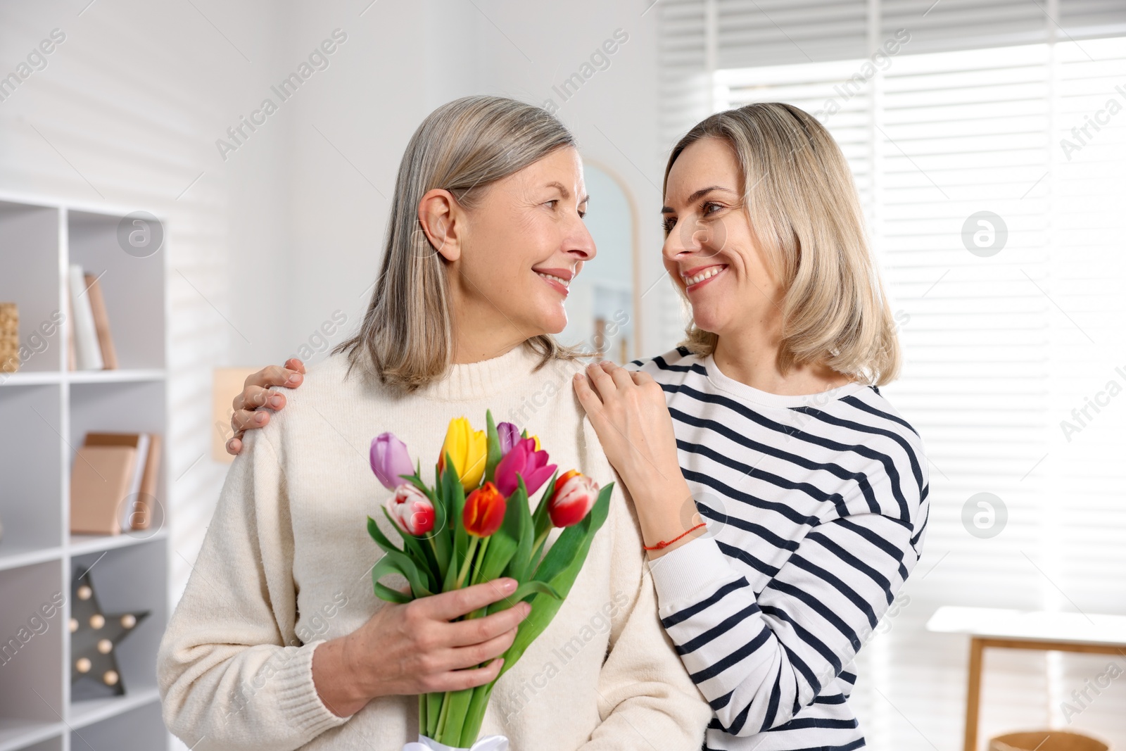 Photo of Smiling woman with bouquet of tulips and her daughter at home. Happy Mother's Day