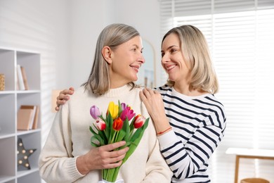 Photo of Smiling woman with bouquet of tulips and her daughter at home. Happy Mother's Day