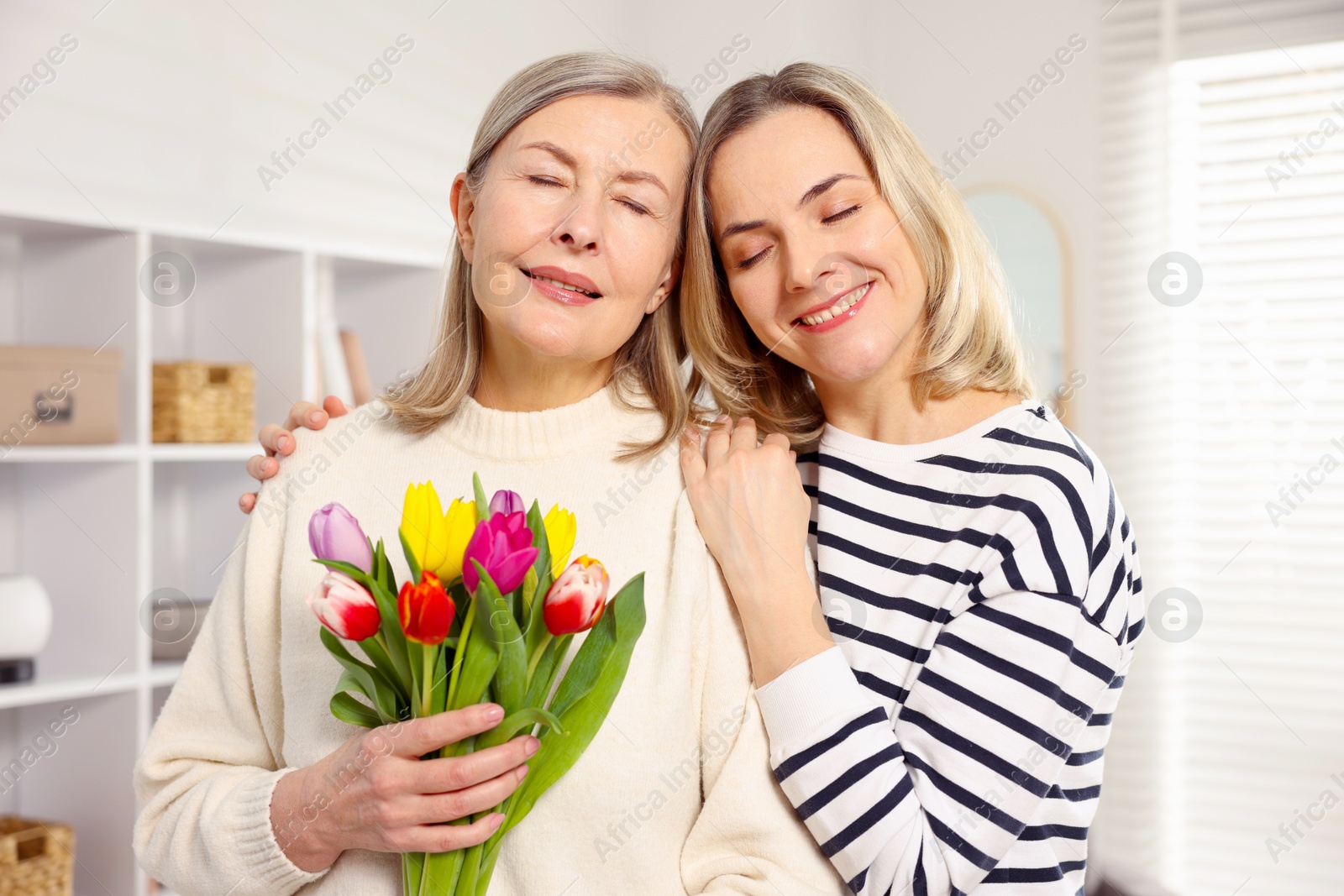 Photo of Smiling woman with bouquet of tulips and her daughter at home. Happy Mother's Day