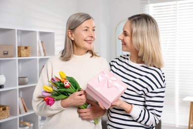 Photo of Smiling daughter congratulating her mom with bouquet of tulips and gift at home. Happy Mother's Day