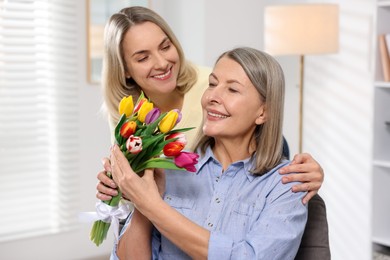 Photo of Smiling daughter congratulating her mom with bouquet of tulips at home. Happy Mother's Day