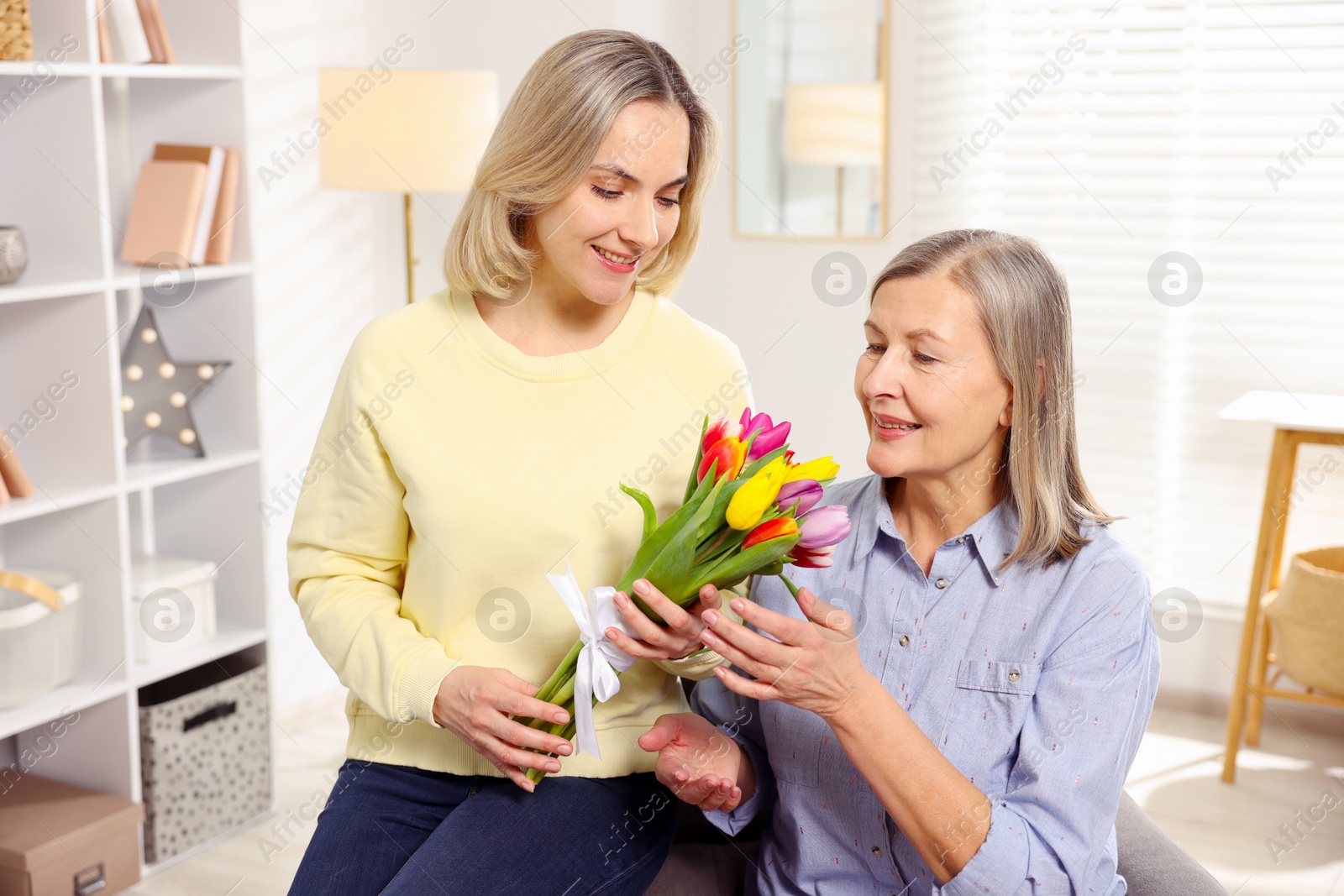 Photo of Smiling daughter congratulating her mom with bouquet of tulips at home. Happy Mother's Day