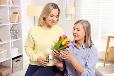 Photo of Smiling daughter congratulating her mom with bouquet of tulips at home. Happy Mother's Day