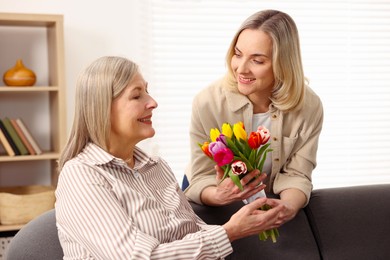 Photo of Smiling daughter congratulating her mom with bouquet of tulips at home. Happy Mother's Day