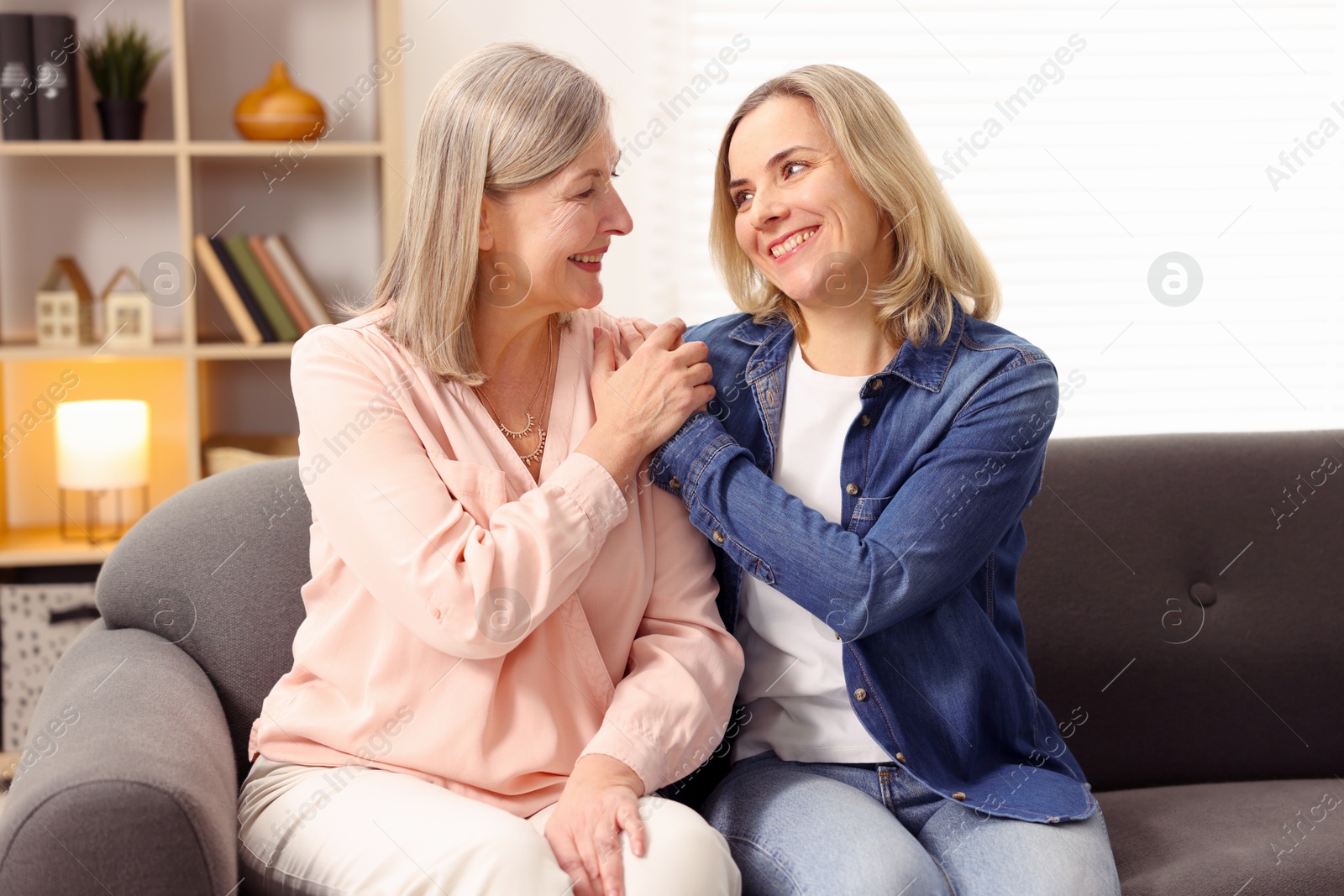 Photo of Smiling mother and her daughter on sofa at home