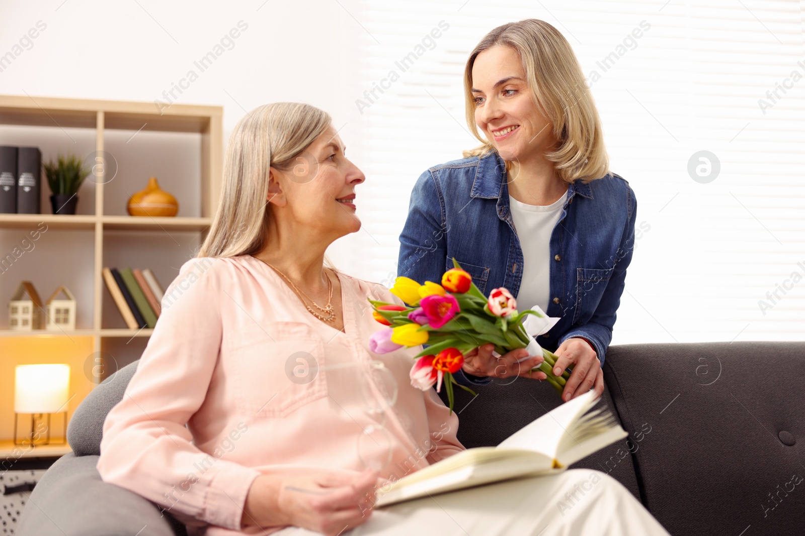 Photo of Smiling daughter congratulating her mom with bouquet of tulips at home. Happy Mother's Day