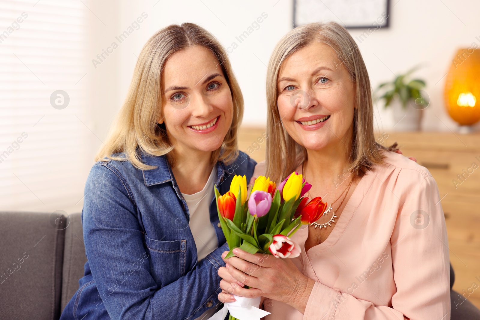 Photo of Smiling woman with bouquet of tulips and her daughter at home. Happy Mother's Day