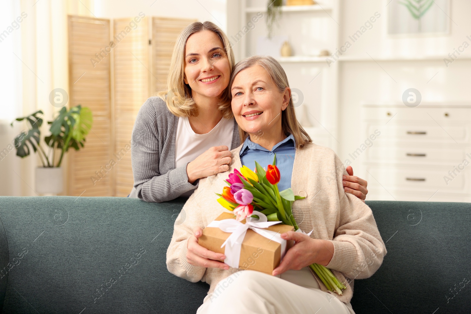 Photo of Family portrait of smiling woman with bouquet of tulips and her daughter at home. Happy Mother's Day