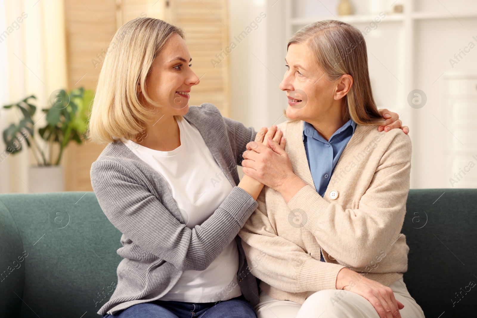 Photo of Smiling daughter and her mother on sofa at home