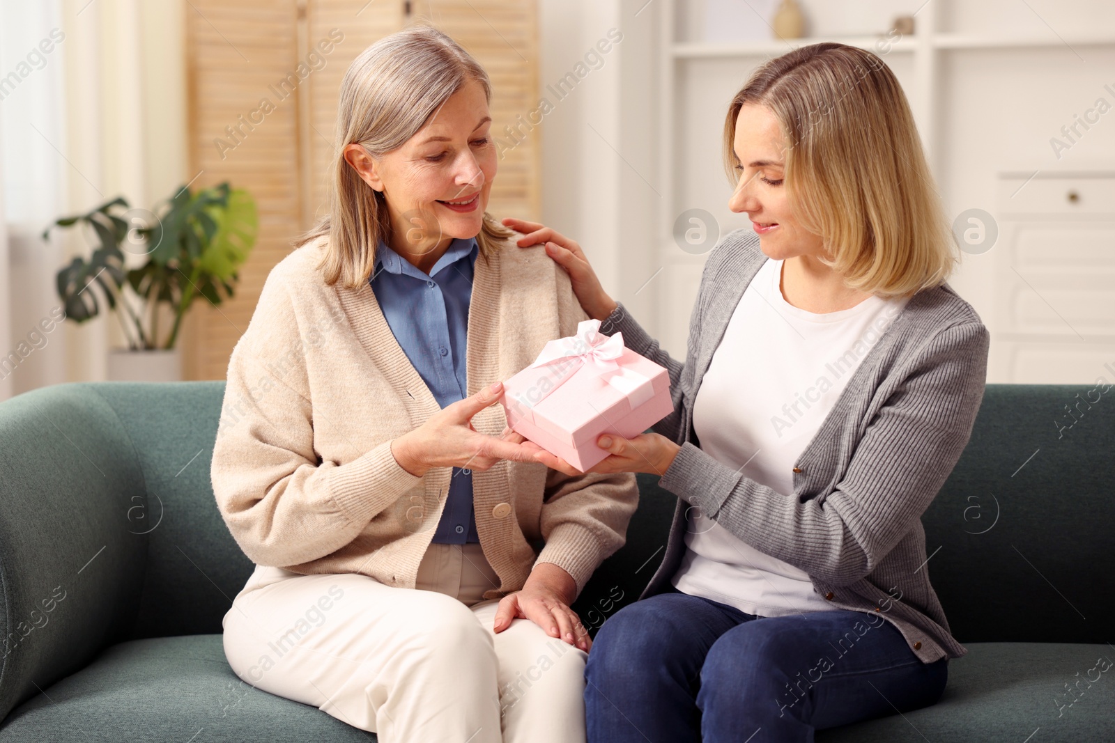 Photo of Daughter congratulating her mom with gift on sofa at home. Happy Mother's Day