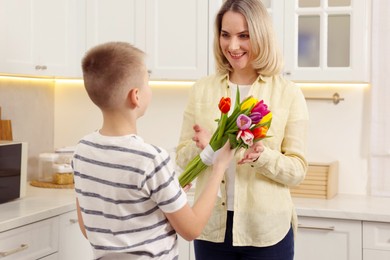 Photo of Happy Mother's Day. Son greeting his mom with flowers in kitchen