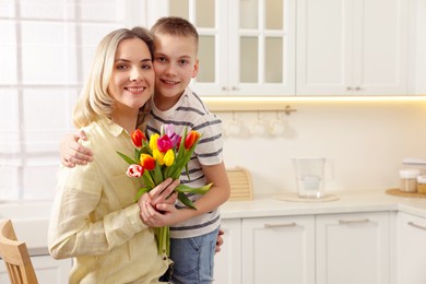 Photo of Happy Mother's Day. Son greeting his mom with flowers in kitchen. Space for text