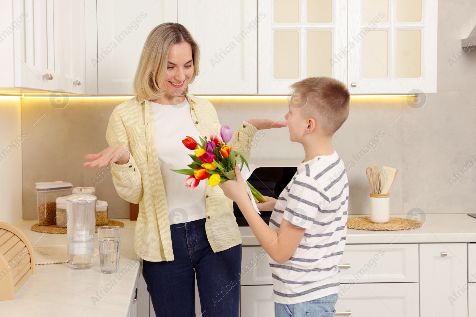 Photo of Happy Mother's Day. Son surprising his mom with flowers in kitchen