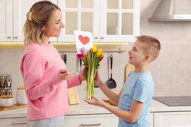 Photo of Happy Mother's Day. Son greeting his mom with flowers and card in kitchen