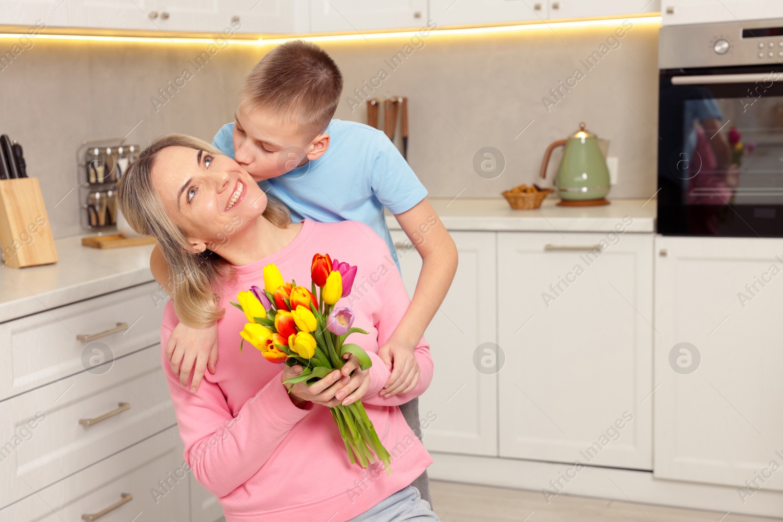 Photo of Happy Mother's Day. Son greeting his mom with flowers in kitchen. Space for text