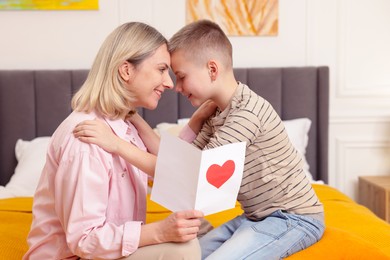 Photo of Happy Mother's Day. Son greeting his mom with card on bed indoors