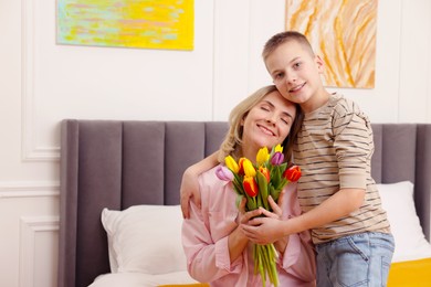 Photo of Happy Mother's Day. Son greeting his mom with flowers at home. Space for text