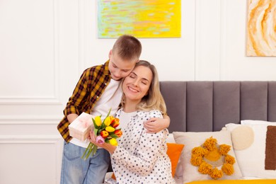 Photo of Happy Mother's Day. Son surprising his mom with gift and flowers at home. Space for text