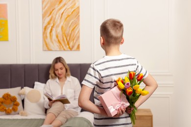 Photo of Happy Mother's Day. Son surprising his mom with gift and flowers at home, selective focus