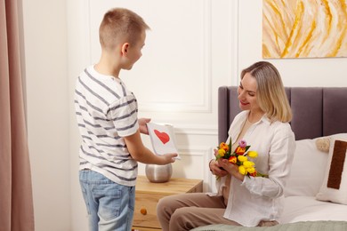 Photo of Happy Mother's Day. Son greeting his mom with flowers and card at home