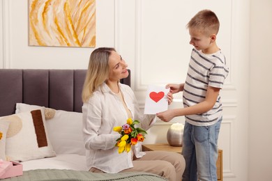 Photo of Happy Mother's Day. Son greeting his mom with flowers and card at home