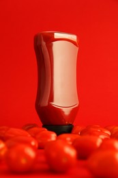 Photo of Bottle of ketchup and tomatoes on red background