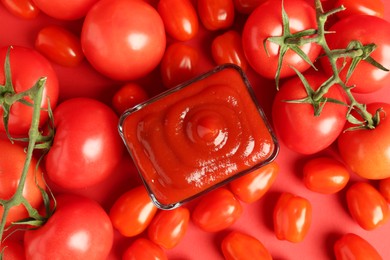 Photo of Ketchup in bowl and tomatoes on red background, top view