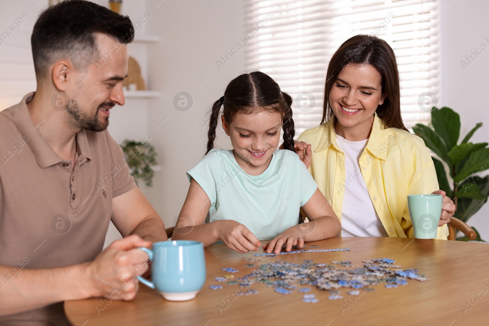 Photo of Happy parents and their daughter solving puzzle together at wooden table indoors