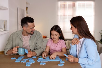 Photo of Happy parents and their daughter solving puzzle together at wooden table indoors