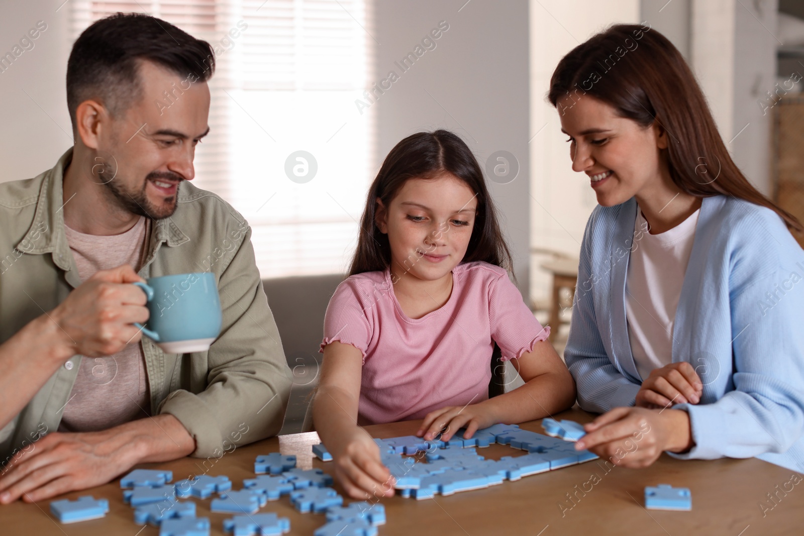 Photo of Happy parents and their daughter solving puzzle together at wooden table indoors