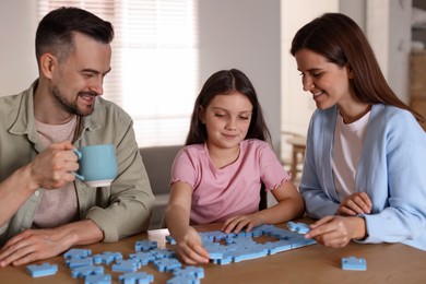 Photo of Happy parents and their daughter solving puzzle together at wooden table indoors