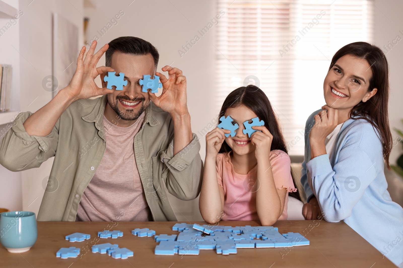 Photo of Happy parents with their daughter having fun and solving puzzle together at wooden table indoors