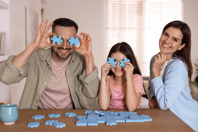 Photo of Happy parents with their daughter having fun and solving puzzle together at wooden table indoors