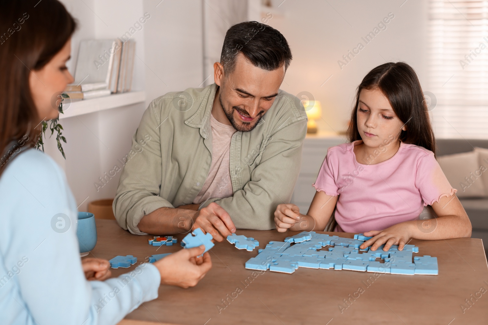 Photo of Happy parents and their daughter solving puzzle together at wooden table indoors