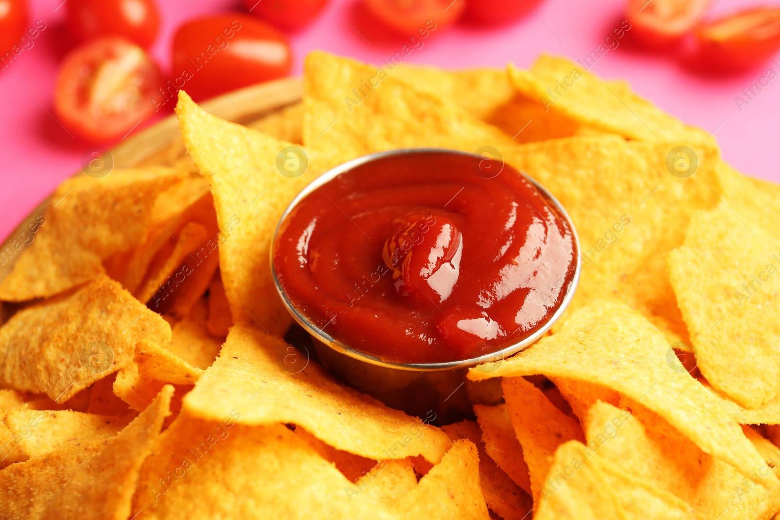 Photo of Tasty ketchup in bowl with nachos on pink background, closeup