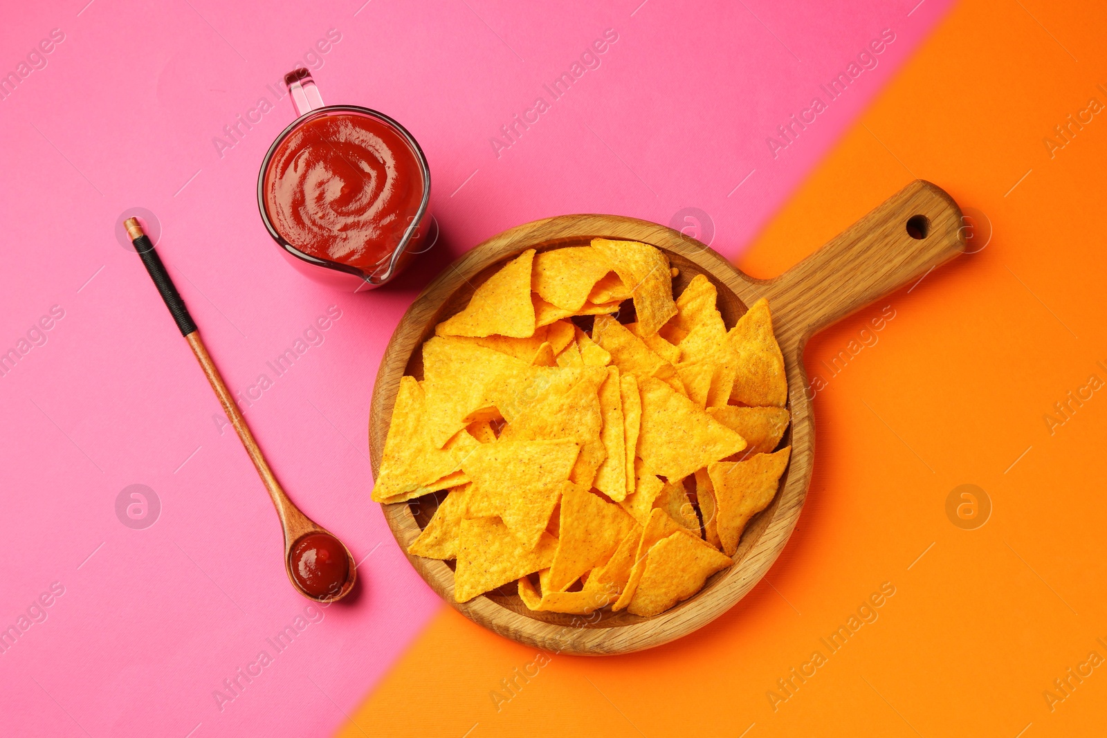 Photo of Tasty ketchup and nachos on pink background, flat lay