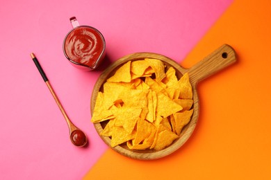 Photo of Tasty ketchup and nachos on pink background, flat lay