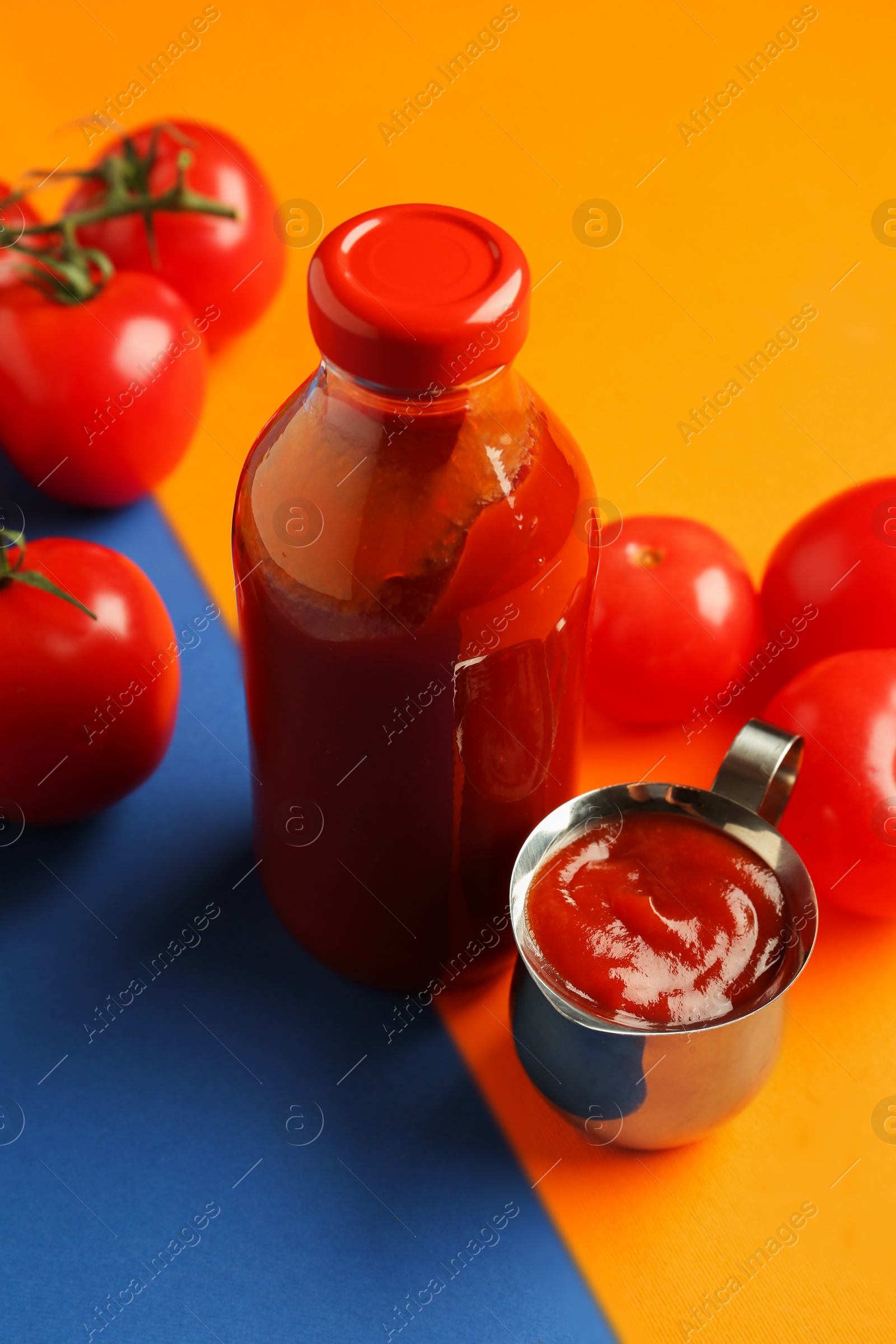 Photo of Tasty ketchup and tomatoes on color background, closeup