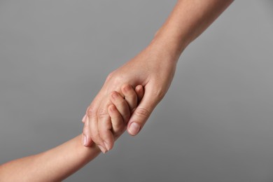 Photo of Mother and child holding hands on grey background, closeup