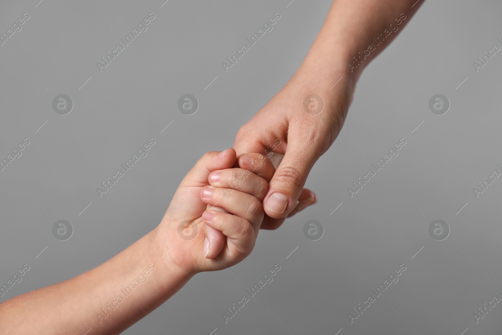 Photo of Mother and child holding hands on grey background, closeup