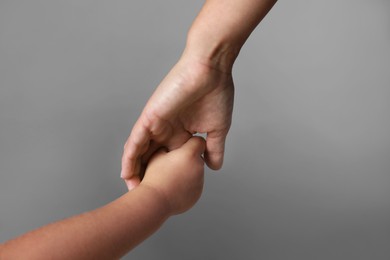 Photo of Mother and child holding hands on grey background, closeup