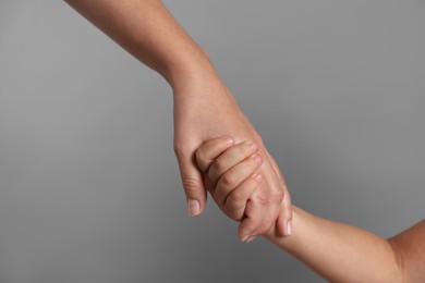 Photo of Mother and child holding hands on grey background, closeup