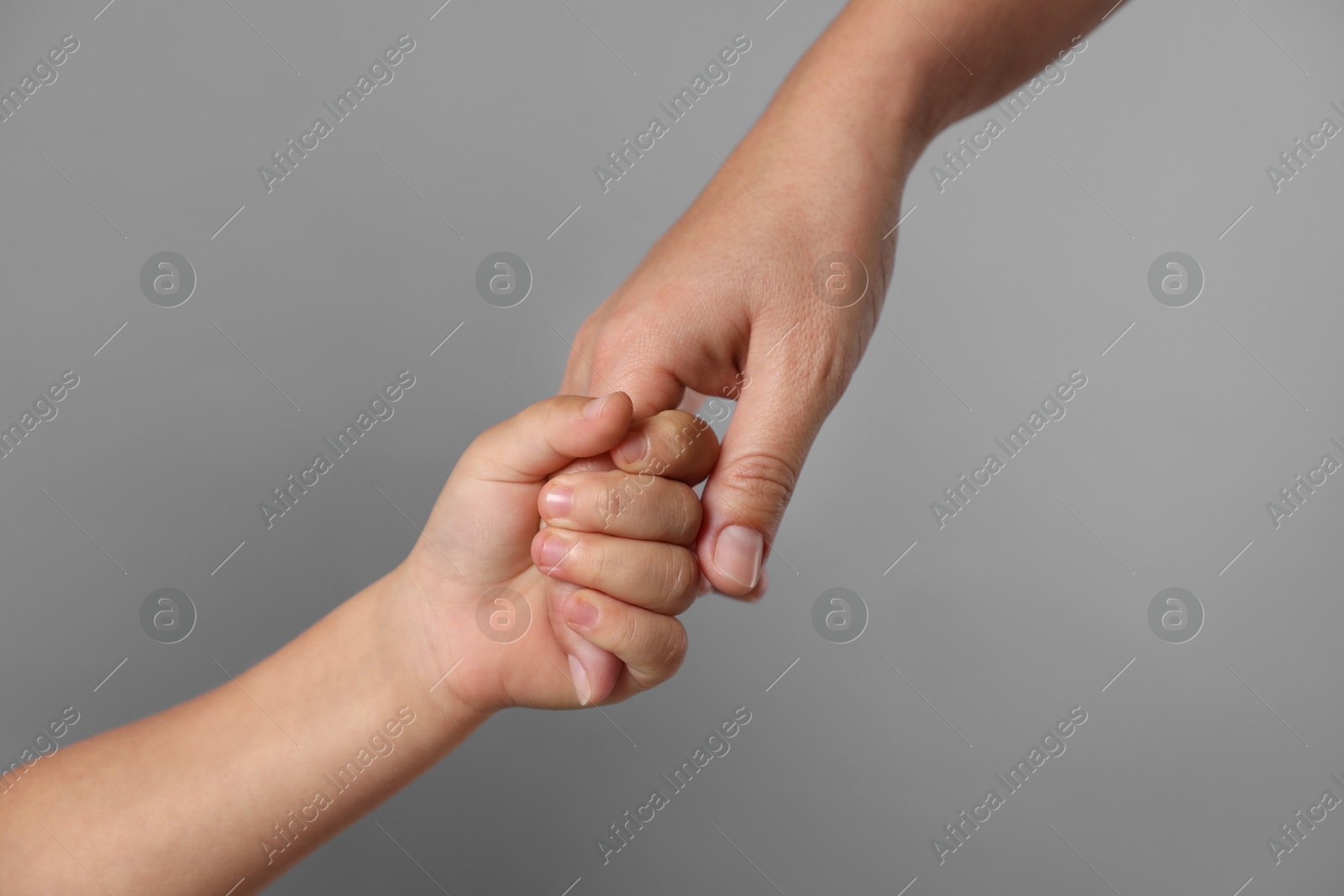 Photo of Mother and child holding hands on grey background, closeup