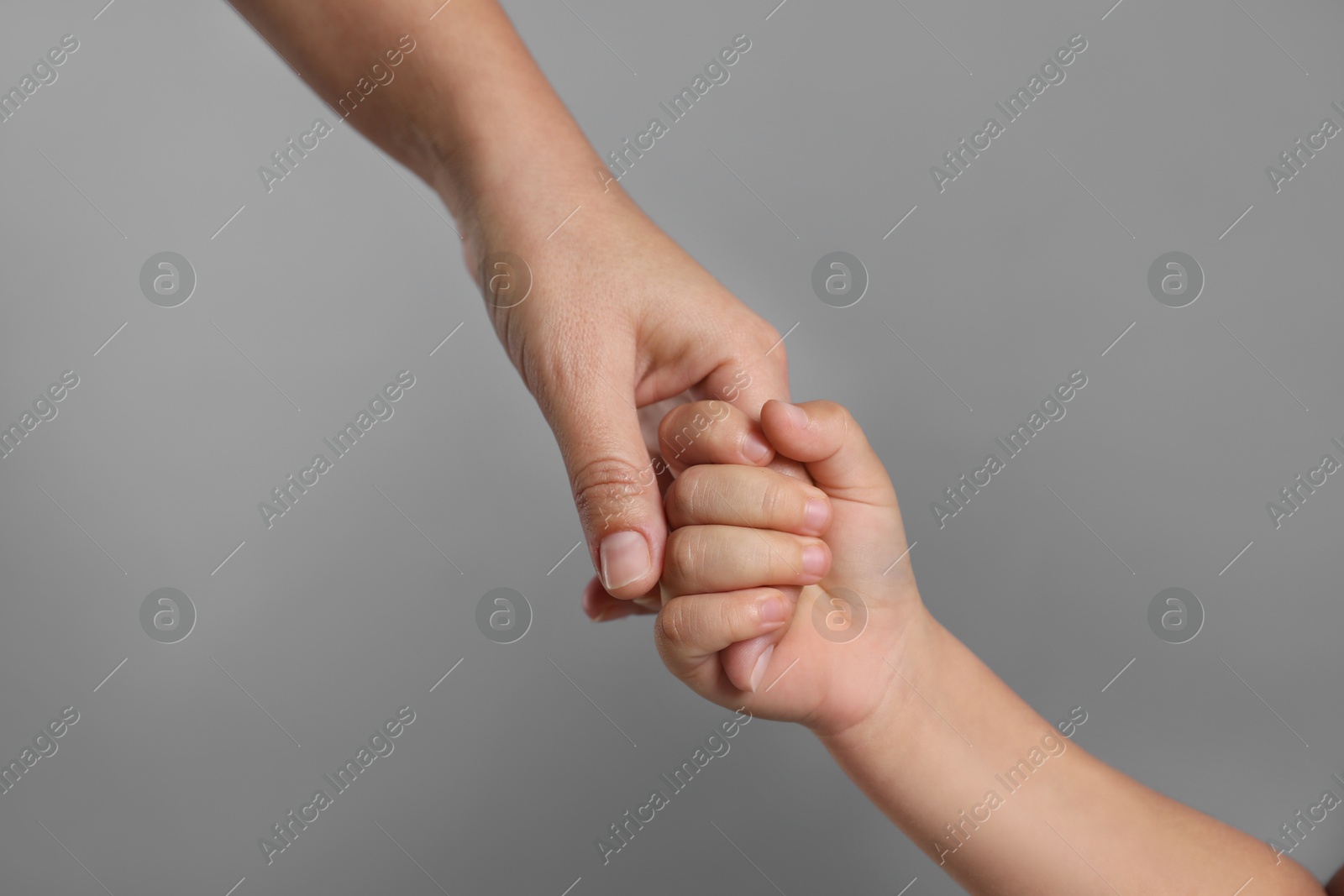 Photo of Mother and child holding hands on grey background, closeup