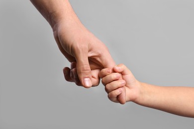 Photo of Father and child holding hands on grey background, closeup