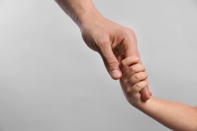 Photo of Father and child holding hands on grey background, closeup. Space for text