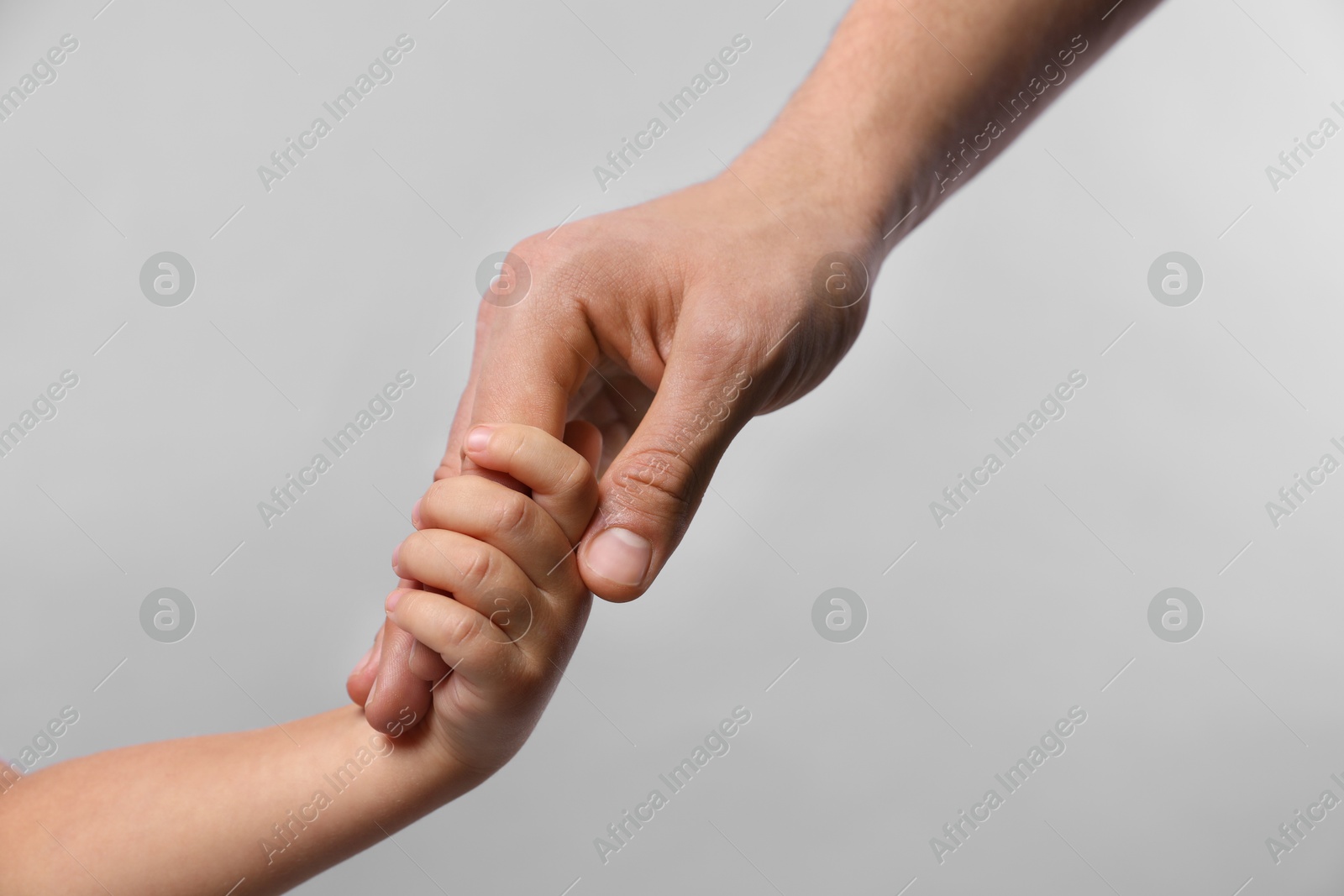 Photo of Father and child holding hands on grey background, closeup