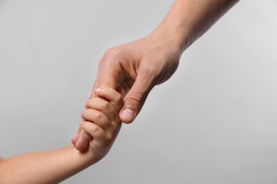 Photo of Father and child holding hands on grey background, closeup