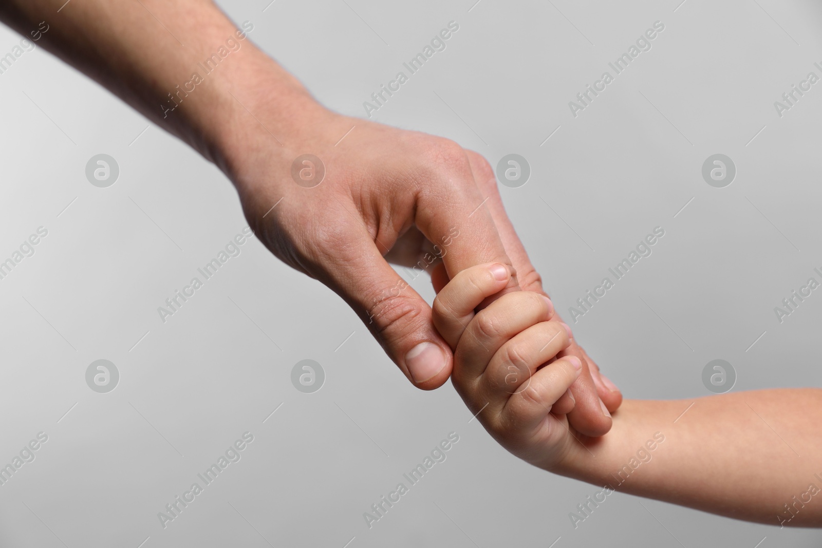 Photo of Father and child holding hands on grey background, closeup