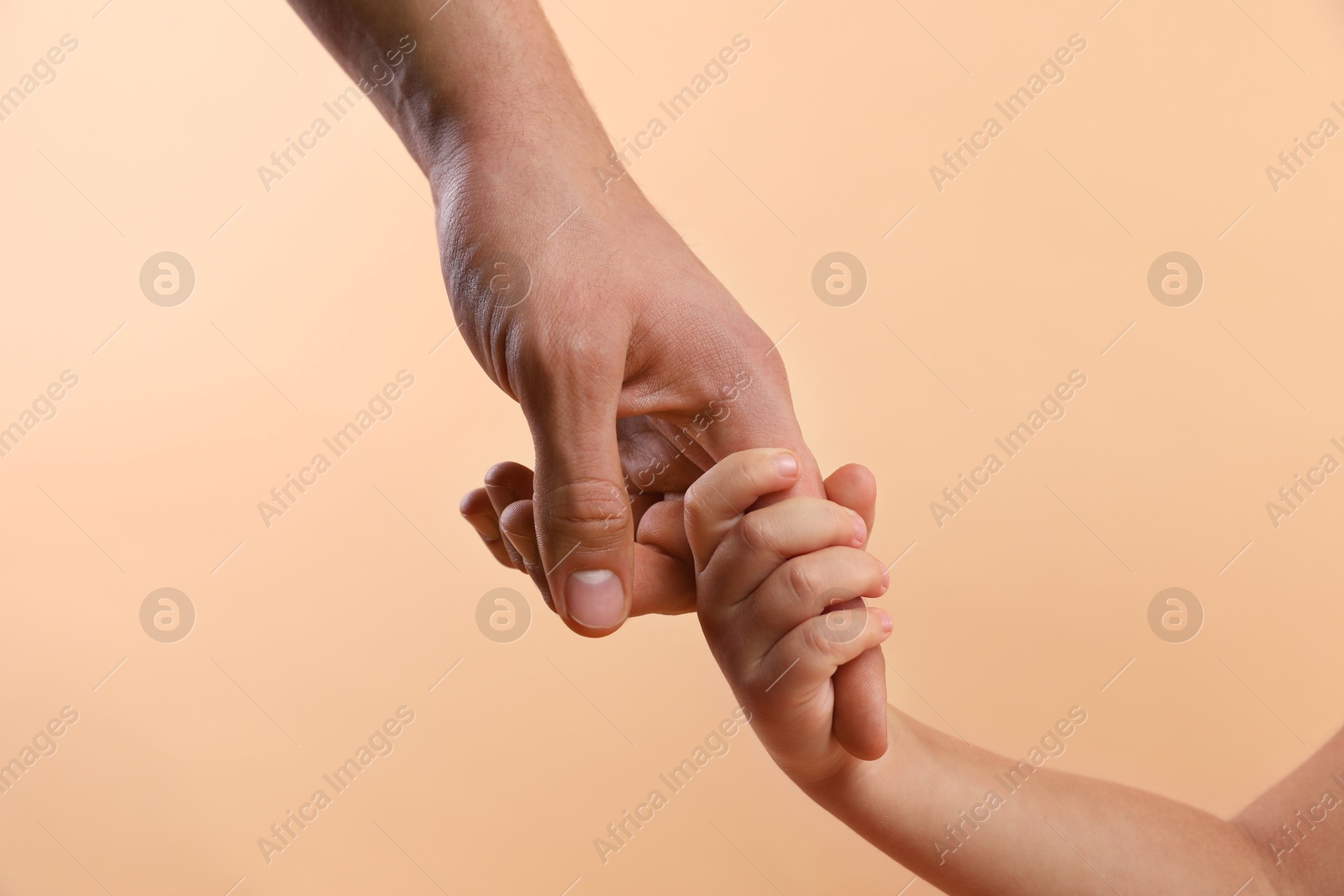 Photo of Father and child holding hands on beige background, closeup